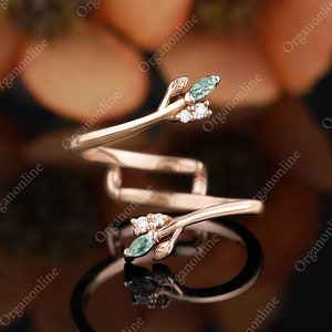 May include: A delicate gold ring with a twisted band and two small green gemstones set in leaf-shaped prongs. The ring features a delicate branch design with small white gemstones.