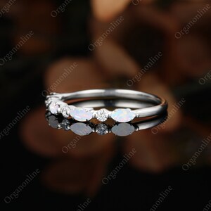May include: A delicate silver band with a row of oval-shaped opals and small round diamonds set in a prong setting.
