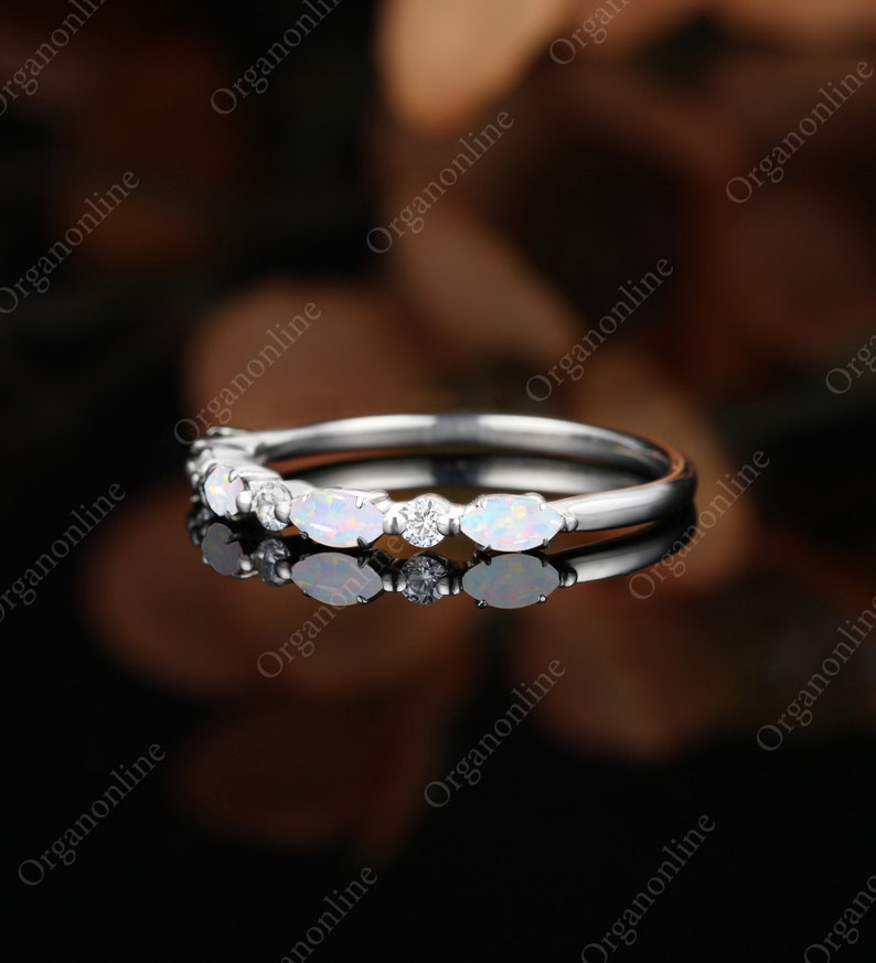 May include: A delicate silver band with a row of oval-shaped opals and small round diamonds set in a prong setting.