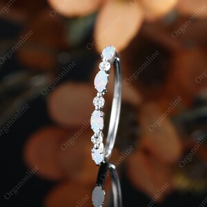May include: A delicate silver band with a row of oval-shaped white opals and small round diamonds.