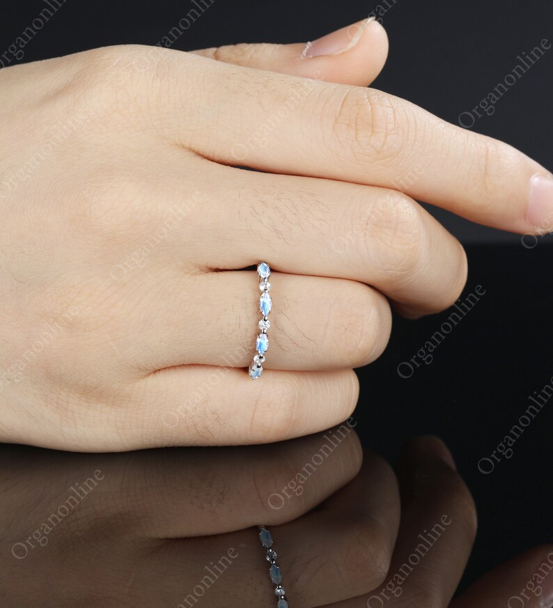 May include: A delicate silver band ring with a row of oval-shaped moonstone gemstones.