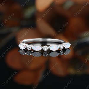 May include: A delicate silver band ring with a row of oval-shaped white opals and small round clear diamonds.