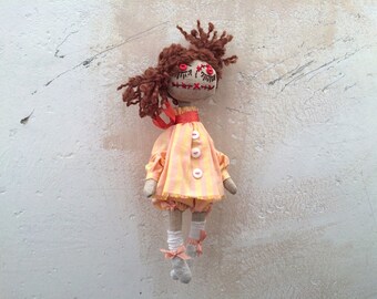 May include: A handmade rag doll with brown yarn hair, a yellow and pink gingham dress, and red buttons. The doll has red embroidered eyes and a stitched mouth.