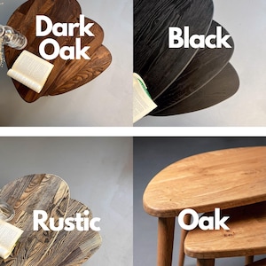 Collage showing four finish options of a handcrafted solid wood nesting table set with organically shaped tops and tapered legs. Variants include dark oak, black, rustic textured wood, and natural oak, each highlighting unique grain patterns and tones. Top-down and angled views emphasize smooth rounded edges and layered nesting design, with styled elements like a book and glass accent enhancing the warm, modern presentation.