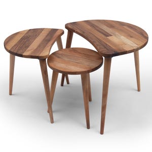 May include: Set of three wooden nesting tables. The tables have a natural wood finish with varying shades of brown. Each table has a unique shape, including a half-moon and a circle, and is supported by three slender, tapered legs.