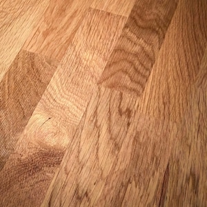 Close-up detail of solid oak wood surface highlighting rich natural grain patterns, varied tonal contrasts, and authentic texture. The panel construction reveals carefully joined sections with visible growth rings, subtle knots, and organic imperfections. Warm honey-brown tones are enhanced by smooth finishing, emphasizing the durability and real wood character suitable for handcrafted furniture design.