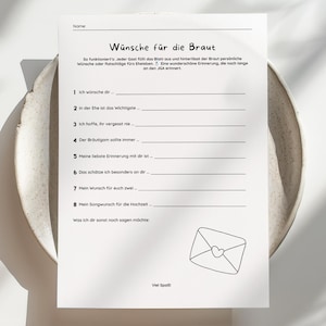 Könnte beinhalten: Ein weißes Papier mit dem deutschen Text „Wünsche für die Braut“ (Wünsche für die Braut), das auf einer hellfarbigen, flachen Schale liegt. Das Papier hat Linien zum Schreiben und eine kleine Umschlagillustration.