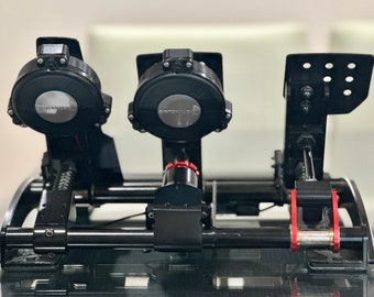 May include: Black racing simulator pedals with a metal frame and red accents. The pedals have a spring-loaded design and are adjustable. The pedals are labeled "Simucube".