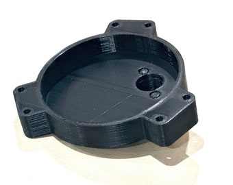May include: A black plastic 3D printed part with a circular opening and multiple holes. The part has a smooth, rounded surface and a textured, layered appearance.