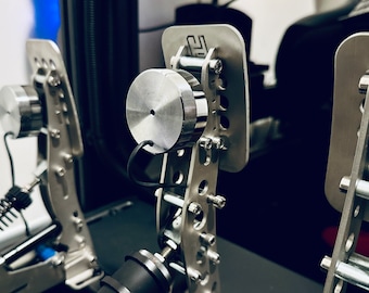 May include: Close-up of a silver metal racing pedal set with a black background. The pedals have a textured surface and are connected by a metal bar. The pedals are designed for use with a racing simulator.