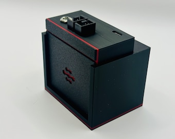 May include: A black box with a red trim and a small black connector on the top. The box has a logo of a stylized wave on the front.