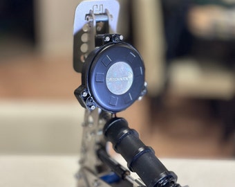 May include: A silver and black drum pedal with a black footboard and a silver spring. The pedal has a black round control knob with the text "Dayton Audio" printed on it.