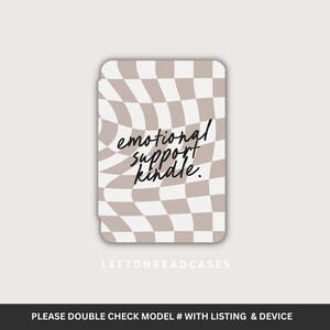 Puede incluir: Una funda para Kindle con un diseño de tablero de ajedrez ondulado en beige y blanco. La funda presenta el texto "emotional support kindle" en un estilo manuscrito. La marca "LEFTONREADCASES" está impresa en la parte inferior.