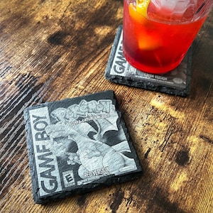 May include: Black and white Game Boy themed coaster with the text "Gotta catch 'em all!" and "Red Version".