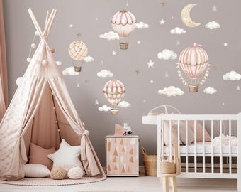 May include: A nursery room with a teepee tent, a crib, and a side table. The walls are decorated with pink and gold hot air balloon wall decals, clouds, and stars.