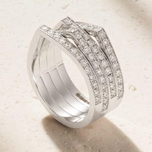 Pu&ograve; includere: Un anello d'argento con pi&ugrave; fasce, ciascuna incastonata con piccole gemme scintillanti. L'anello ha un design moderno con linee pulite e una finitura lucida. Le gemme sono uniformemente distanziate e catturano la luce, creando un effetto brillante.