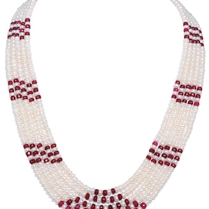 Może przedstawiać: Wielorzędowy naszyjnik z pereł z czerwonymi akcentami z kamieni szlachetnych. Naszyjnik wykonany jest z białych pereł i czerwonych kamieni szlachetnych i jest ułożony w warstwowym wzorze.