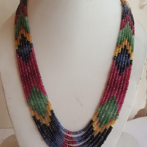 May include: A multi-strand necklace made of small, faceted gemstones. The necklace features a repeating pattern of red, green, blue, and yellow gemstones.