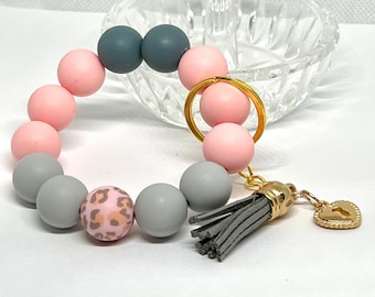 May include: A pink, gray, and leopard print silicone beaded keychain with a gold key ring and a gray tassel.