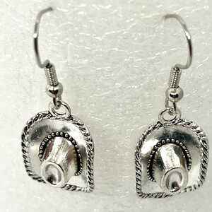 May include: A pair of silver earrings featuring a cowboy hat design. The hats have a detailed, textured design and are attached to silver hooks.