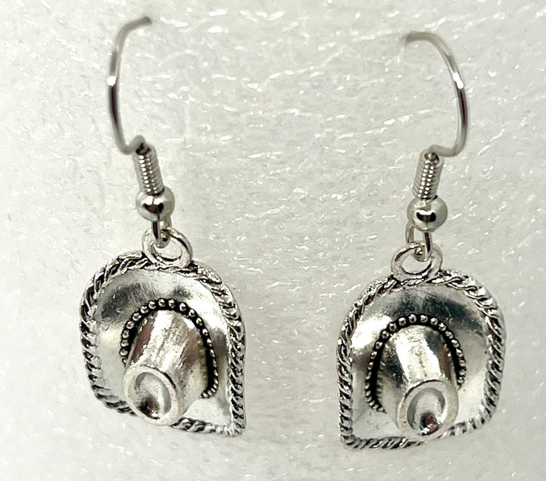 May include: A pair of silver earrings featuring a cowboy hat design. The hats have a detailed, textured design and are attached to silver hooks.