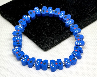 May include: A stretch bracelet featuring blue, controller-shaped beads with printed details including a black plus sign, a red circle, and small white dots. The blue controller beads are separated by small, round, metallic silver-colored spacer beads.
