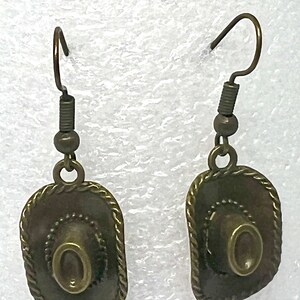 May include: A pair of bronze-colored earrings featuring a cowboy hat design. The hats have a textured, rope-like trim around the edges.