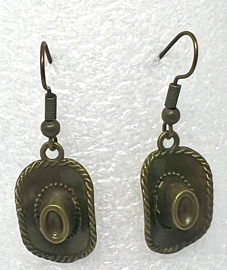 May include: A pair of bronze-colored earrings featuring a cowboy hat design. The hats have a textured, rope-like trim around the edges.