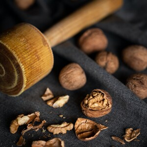 May include: A wooden mallet and a pile of walnuts, some of which are cracked open, on a dark gray fabric surface.