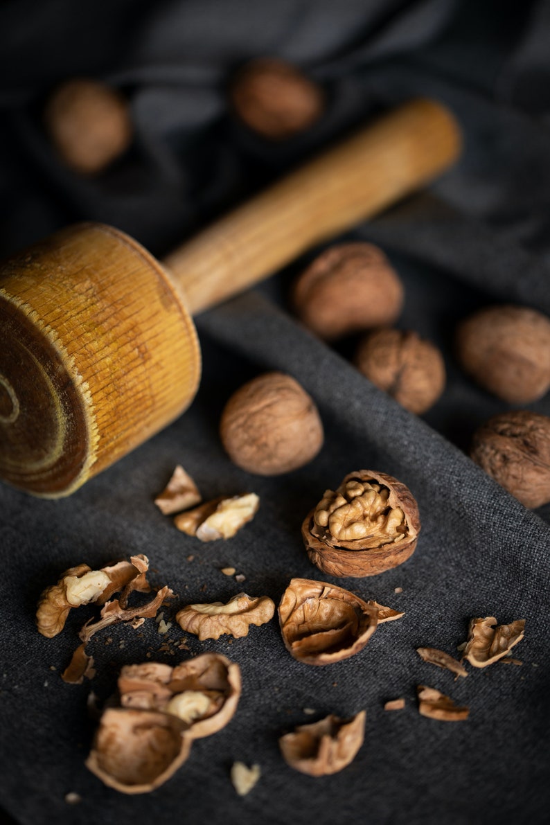 May include: A wooden mallet and a pile of walnuts, some of which are cracked open, on a dark gray fabric surface.