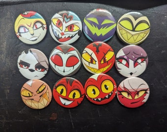 May include: Twelve round pinback buttons featuring cartoon characters with various expressions. The characters have red, yellow, and black eyes, and some have fangs. The buttons are on a dark gray surface.