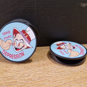 Peut inclure: Deux poignées de téléphone rondes avec un fond bleu et une image de dessin animé d'un personnage avec des cheveux roux et une couronne. Le texte sur la poignée dit "Take that, Depression".