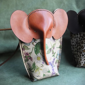 Peut inclure: Un petit sac en cuir marron en forme d'éléphant avec un imprimé floral. Le sac a une longue bandoulière et une petite poche sur le devant.