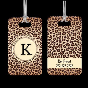May include: A brown and tan leopard print luggage tag with a gold-colored decorative frame and the letter "K" in the center. The tag also includes the text "Kim Frenzel" and a phone number, "222-222-2222".