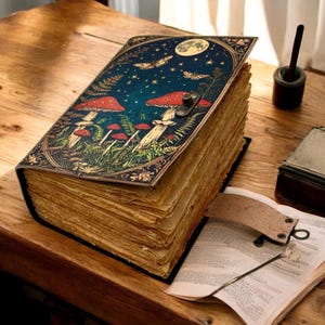 May include: A large, leather-bound journal with a dark blue cover featuring a whimsical illustration of mushrooms, stars, and butterflies. The journal is open to reveal thick, aged pages.