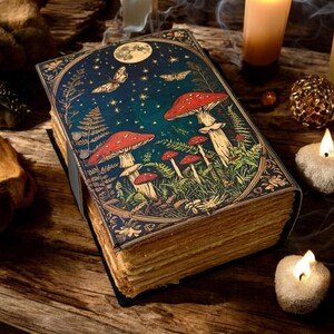 May include: A vintage-style, leather-bound journal with a dark green cover featuring a whimsical illustration of red mushrooms, stars, and a moon in a forest setting.