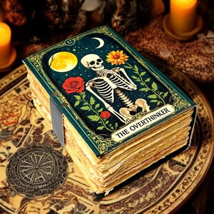 May include: A decorative journal with a dark teal cover featuring a skeleton, moon, and floral elements. The journal's title, "THE OVERTHINKER," is displayed on the cover. The pages are aged, and the journal is bound with a grey ribbon.