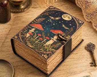 May include: A rectangular journal with a dark blue cover featuring a moon, stars, butterflies, and red mushrooms. The book has a brass-coloured metal latch closure and thick, textured, light brown paper pages with deckled edges.