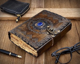 May include: A brown leather journal with intricate embossed designs and a blue gemstone accent. The journal has a brass clasp and is closed.
