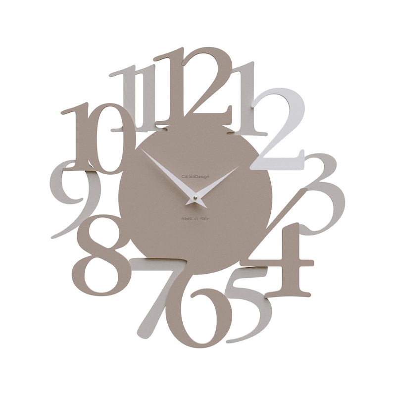 May include: A modern wall clock with a taupe-colored face and white hands. The numbers are in a unique, overlapping design, with some in white and others in taupe. The clock face has the text "CallesDesign" and "made in italy".
