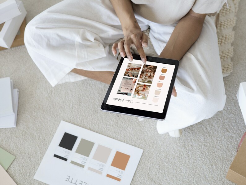 May include: A person is reviewing a color palette on a tablet. The tablet screen shows a color palette with different shades of brown and beige. The person is sitting on a carpet and has a piece of paper with a color palette on it.
