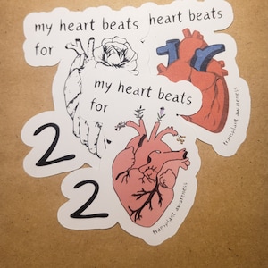 May include: Four stickers with the text "my heart beats for" and a stylised image of a heart. Two of the stickers have a red heart with a blue interior, and two have a pink heart with black veins. The text "transplant awareness" is on the bottom of each sticker.