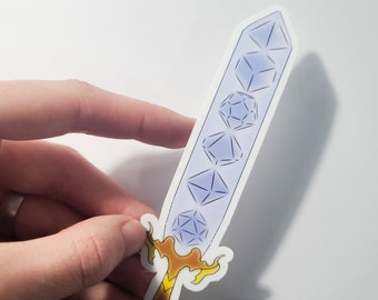 May include: A sticker in the shape of a sword with a light blue blade and a gold hilt. The blade features the shapes of various dice used in tabletop role-playing games. The sticker is held by a hand.