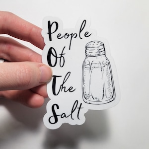 May include: A white sticker featuring the text "People Of The Salt" in black, alongside a line drawing of a salt shaker. The sticker is held by a hand. The design is simple and monochrome.