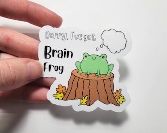 May include: A sticker with a green frog sitting on a tree stump. The frog is thinking and has a thought bubble above its head. The sticker says "Sorry, I've got Brain Frog".