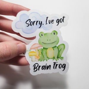 May include: A sticker with a green frog sitting on a mushroom. The sticker says "Sorry, I've got Brain Frog" in a cloud above the frog.