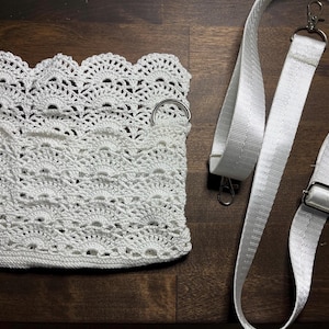 May include: White crocheted bag with two silver metal rings and a white adjustable strap.