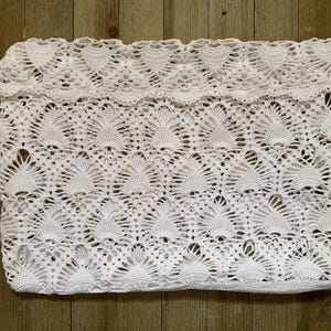 Könnte beinhalten: Weißes Häkelgewebe mit einem zarten, durchbrochenen Muster. Der Stoff hat einen gewellten Rand und ist aus einem feinen, leichten Garn gefertigt.