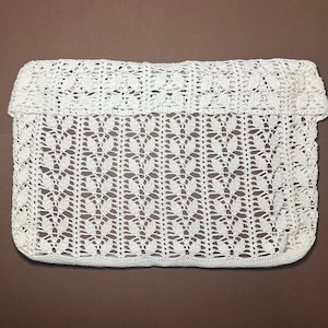 May include: White crocheted bag with a delicate pattern. The bag has a fold-over top and a flat bottom.