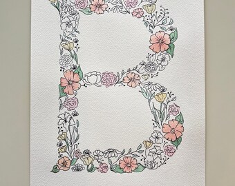 Può includere: Un dipinto ad acquerello della lettera "B" composta da fiori in tonalità di rosa, pesca e giallo. I fiori sono contornati da inchiostro nero.